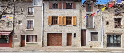 A stone building with wooden shutters, a cobblestone street, and a parked car.