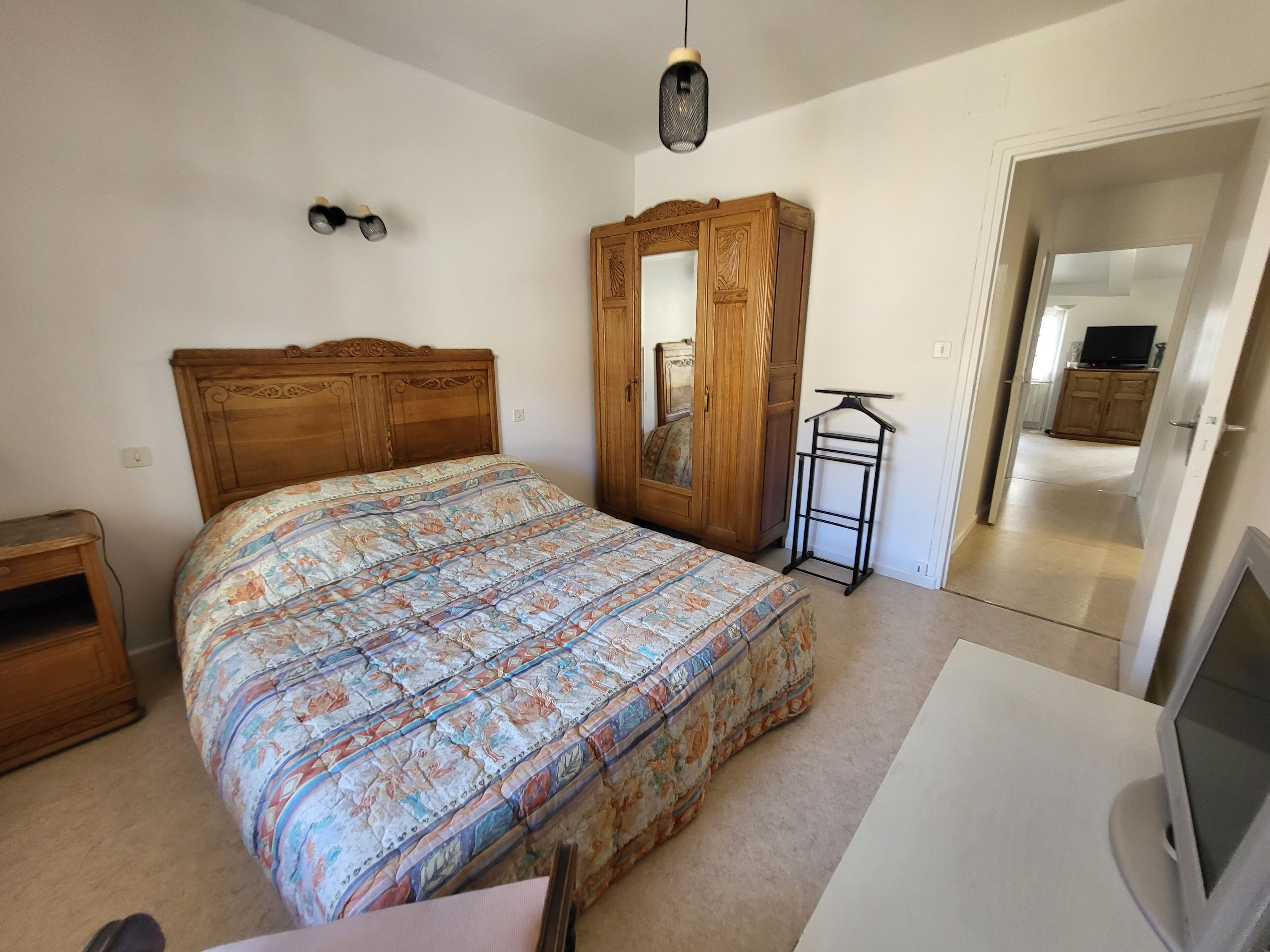A bedroom with a wooden bed, a wardrobe, a hanging rack, and a television.