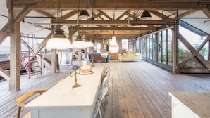 A spacious loft with a high ceiling, exposed wooden beams, and a long wooden deck.