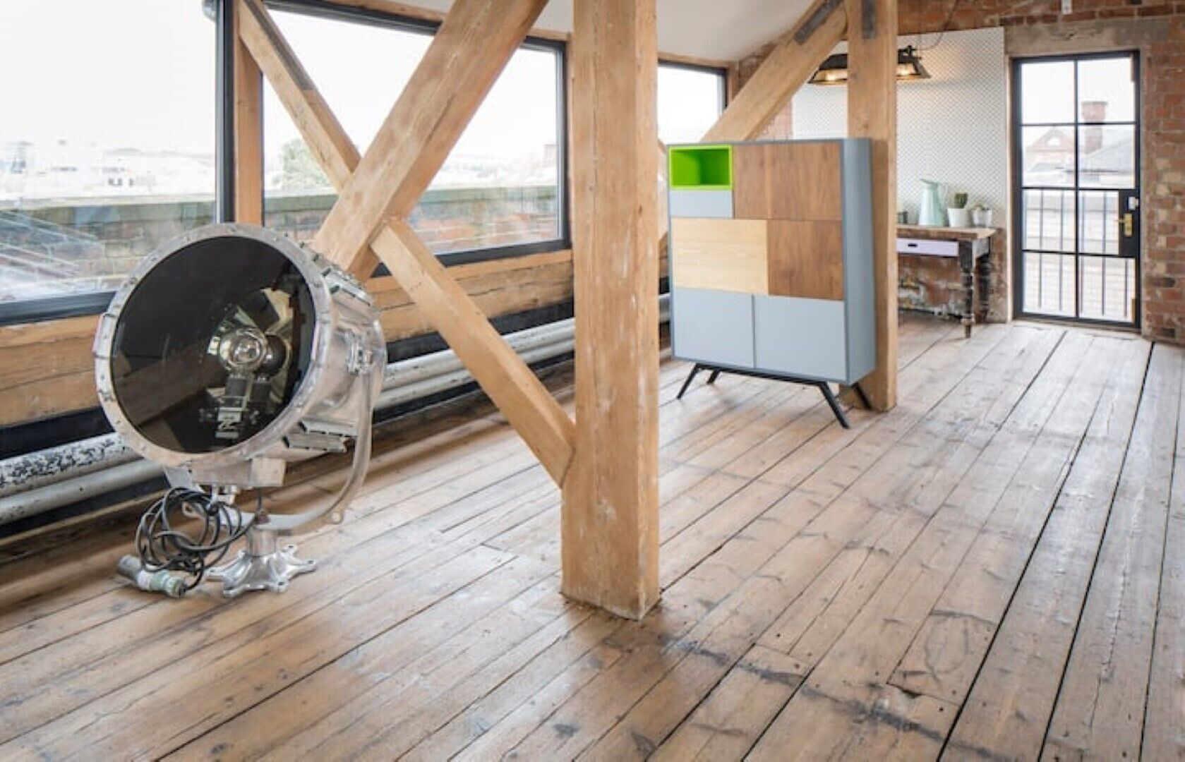 Ein geräumiges Zimmer mit Holzböden, einem großen Fenster und einer modernen Kommode mit grüner Ablagefläche.