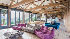 A spacious room with wooden floors, large windows, and a variety of seating including a purple sofa, a floral-patterned sofa, and a blue armchair.