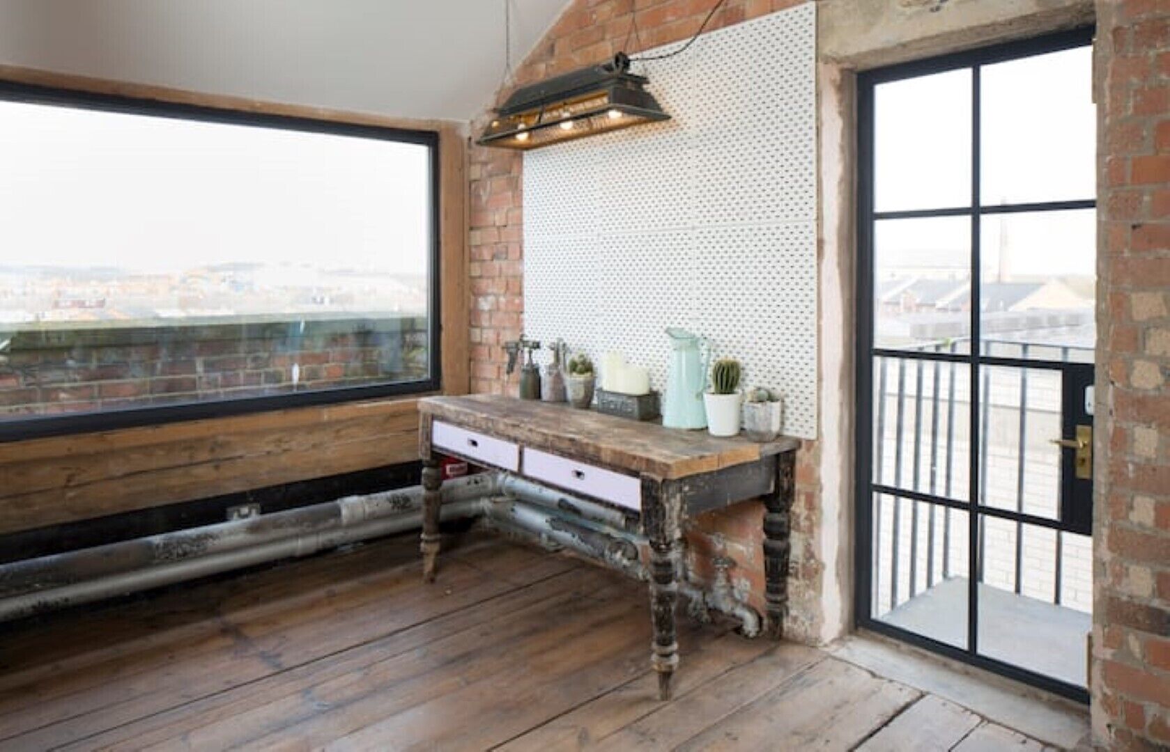 A rustic room with a wooden desk, a large window, and a view of the city.