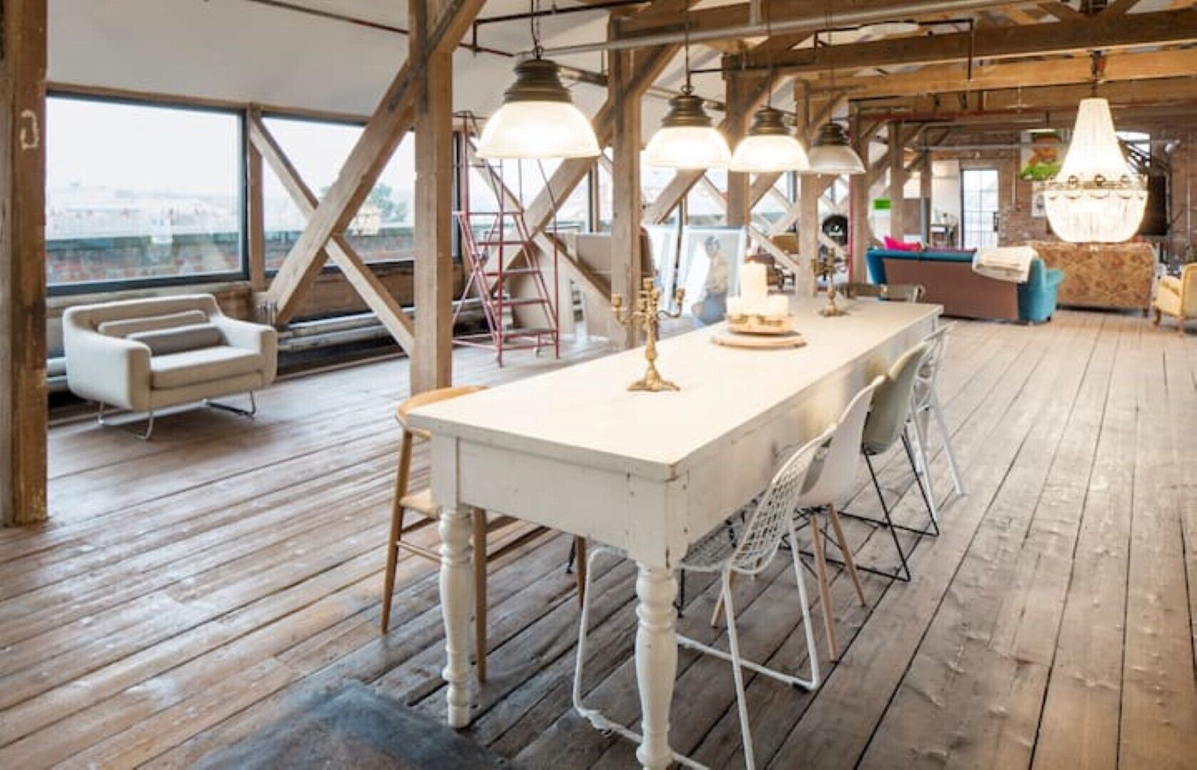 Une pièce spacieuse avec une grande table en bois, des chaises blanches et des lampes suspendues.