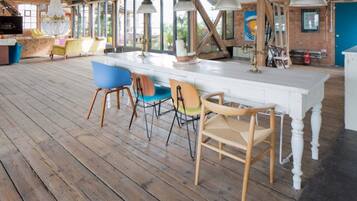 Une pièce spacieuse avec un plancher en bois, une longue table blanche et plusieurs chaises.