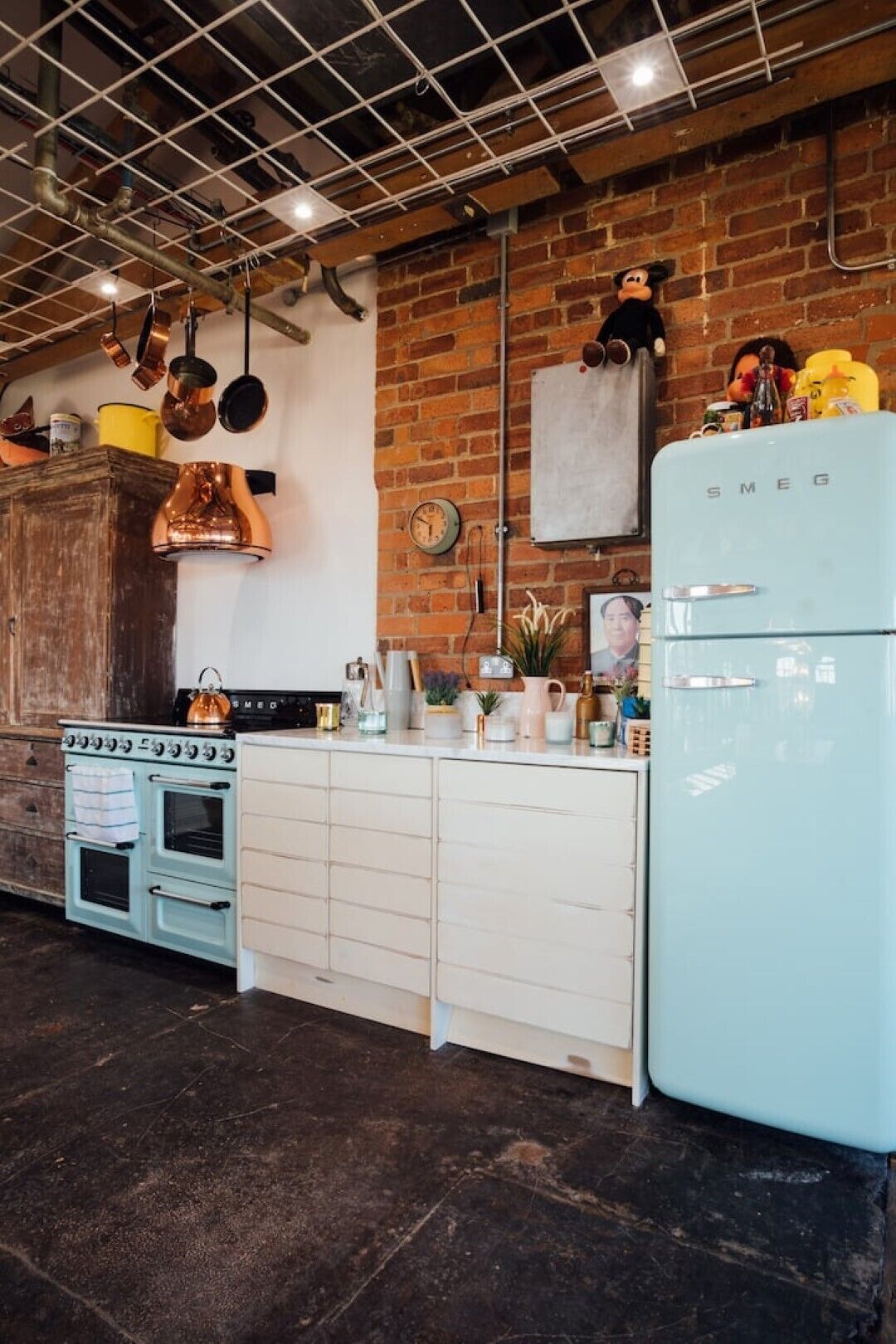 A kitchen with a vintage blue refrigerator, a white stove, and copper cookware hanging from the ceiling.