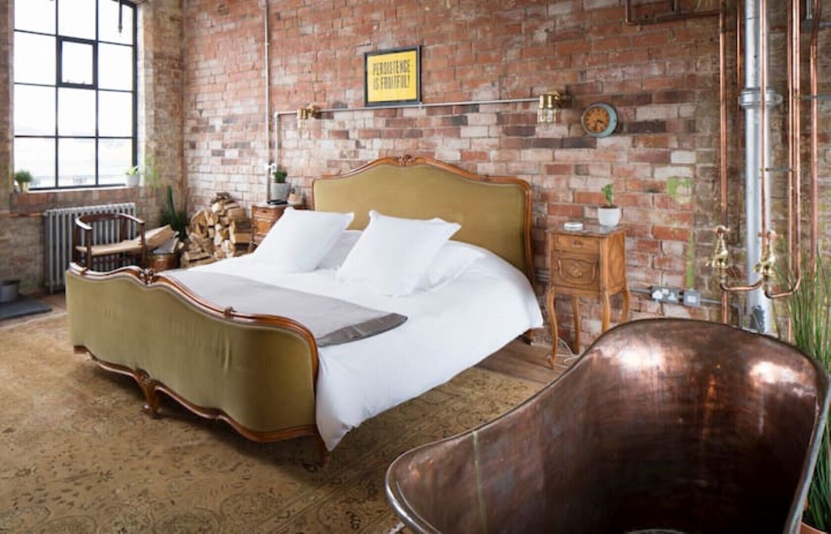A spacious bedroom with a large bed, a vintage chair, and a brick wall.