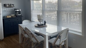 Eine moderne Küche mit einem weißen Tisch, Korbstühlen, einer Pendelleuchte und einem Fenster mit Jalousien.