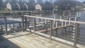 Eine Holzterrasse mit Geländer, die auf ruhiges Wasser blickt, mit Gebäuden im Hintergrund.