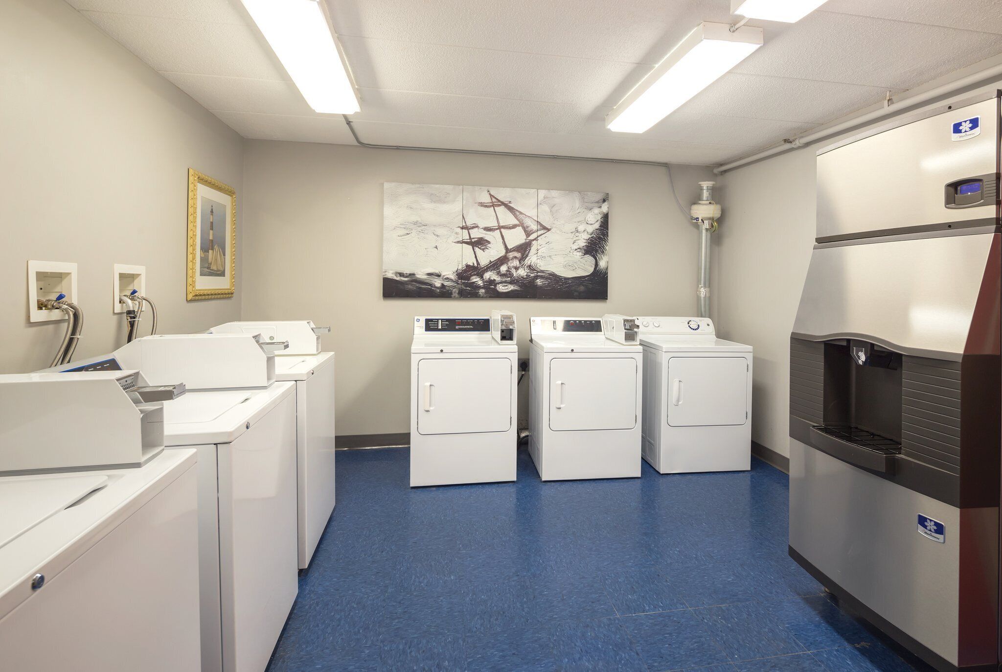A laundry room with four washing machines, a refrigerator, and a large painting on the wall.