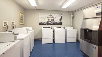 A laundry room with four washing machines, a refrigerator, and a large painting on the wall.