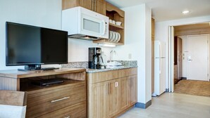 A modern kitchen with wooden cabinets, a microwave, a flat-screen TV, and a coffee maker. - Thames Street - Newport Harbor 1 Bedroom (Newport)