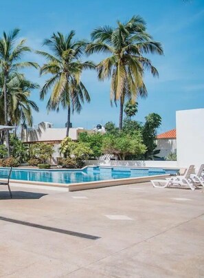 A swimming pool with lounge chairs, surrounded by palm trees and greenery. - Condos HDS (Mazatlán)