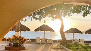 Un espace extérieur aménagé avec des parasols, des chaises et une vue sur la mer au coucher du soleil.