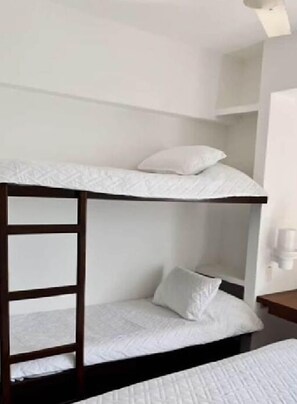 A bunk bed with a wooden ladder, white bedding, and a small bedside table with a lamp.