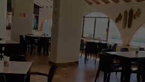 Une salle à manger spacieuse avec de hauts plafonds et des poutres apparentes, comprenant plusieurs tables et chaises.