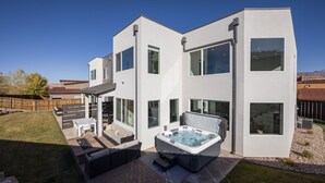 Una casa moderna de dos pisos con jacuzzi, mobiliario exterior y patio cercado.