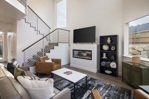 Una sala de estar moderna con una escalera, una chimenea y un ventanal que ofrece vistas al exterior.