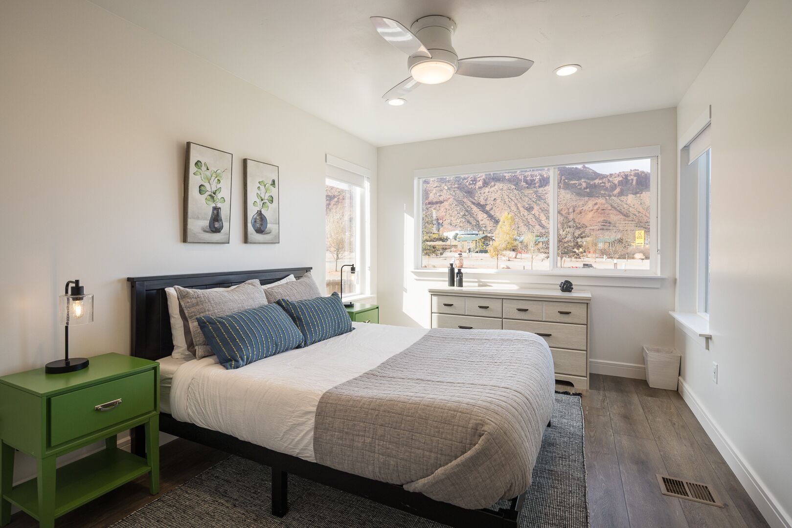 Een slaapkamer met een bed, nachtkastjes, een dressoir en een raam met uitzicht op de bergen.