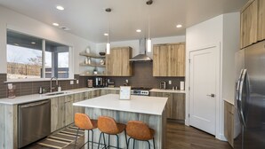 Una cocina moderna con una isla central, taburetes de bar, electrodomésticos de acero inoxidable y armarios de madera.