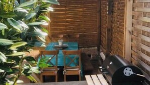 Um pátio externo com mesa e cadeiras de madeira, churrasqueira e área de estar coberta.