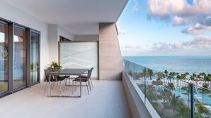 Ein Balkon mit Esstisch und Stühlen, Blick auf einen Pool und den Ozean.