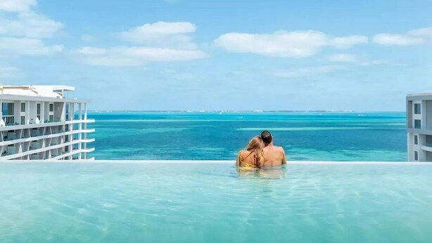 Ein Paar in einem Pool mit bodenlosem Überlauf und Blick auf das Meer und den weiten Horizont.