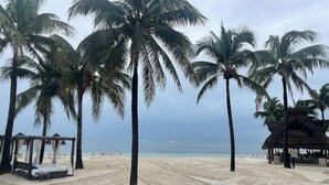 Ein Strand mit Palmen, eine strohgedeckte Hütte und ein Bett mit Baldachin.
