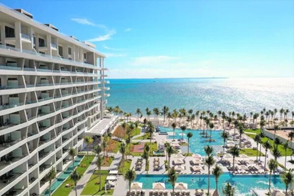 A hotel with multiple floors, a pool area with lounge chairs, and a view of the ocean.