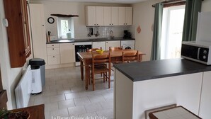 Eine kompakte Küche mit Essbereich, ausgestattet mit einer zentralen Kochinsel, Holzschränken und einem Fenster mit Vorhängen.