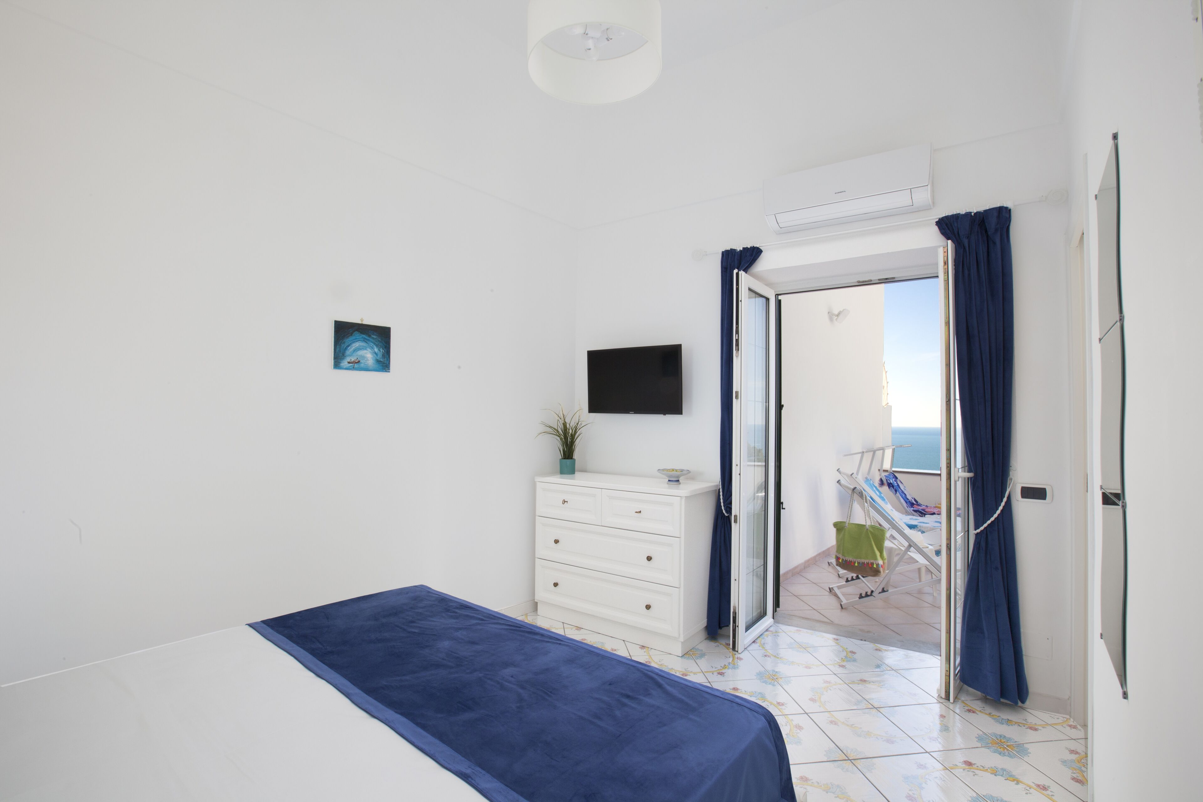 Ein Schlafzimmer mit Bett, Schminktisch, Fernseher und Blick auf einen Balkon.