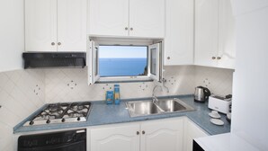 A kitchen with white cabinets, a gas stove, a sink, and a window with a view of the sea.