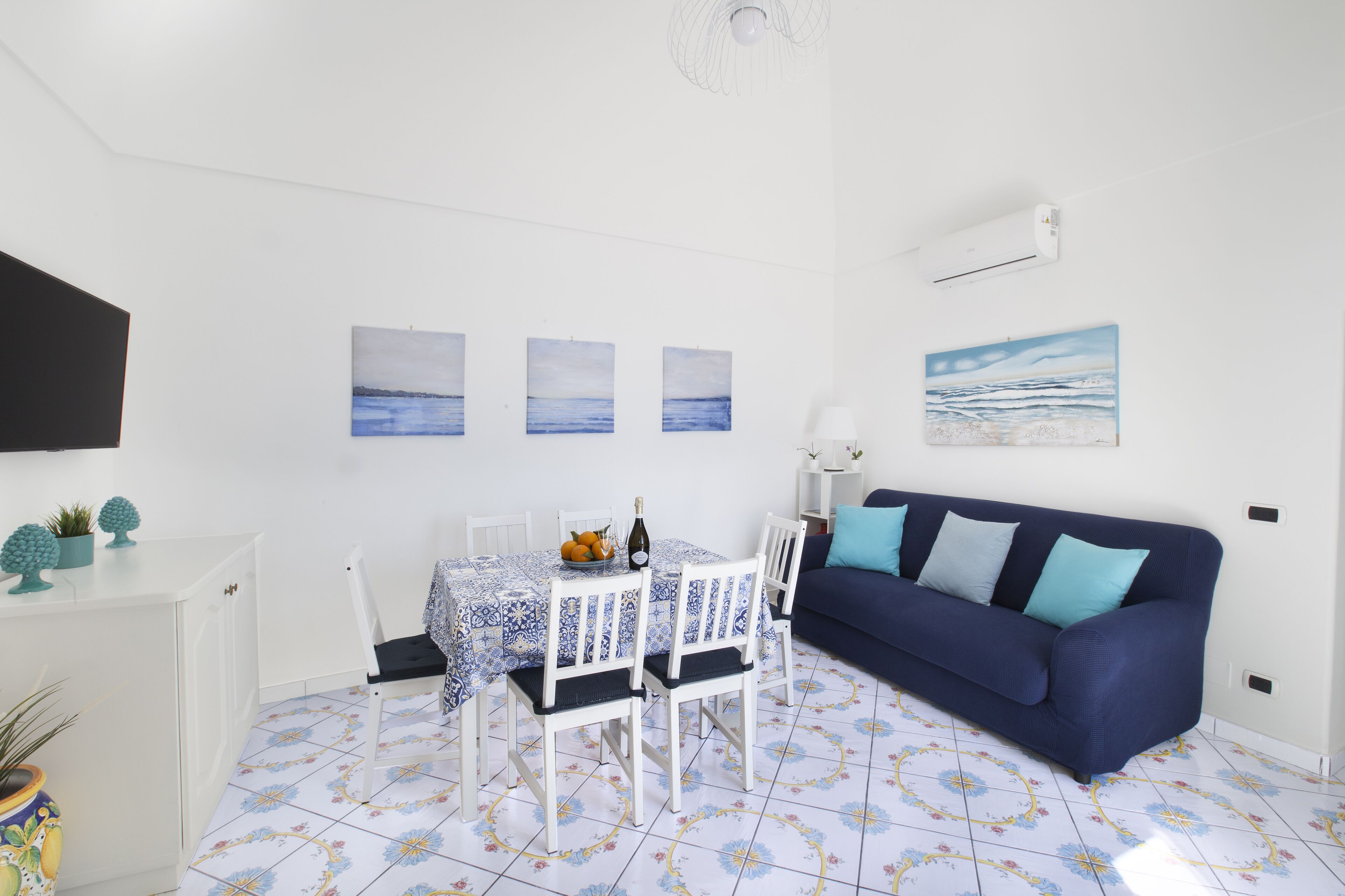 A room with a dining table set with chairs, a blue sofa, and a wall-mounted air conditioner.