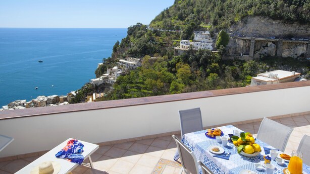 A balcony with a table set for breakfast overlooking a coastal view with buildings and cliffs.