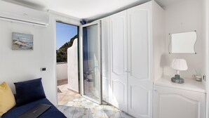 A bedroom with a bed, a laptop, a nightstand with a lamp, and a view of the outside.