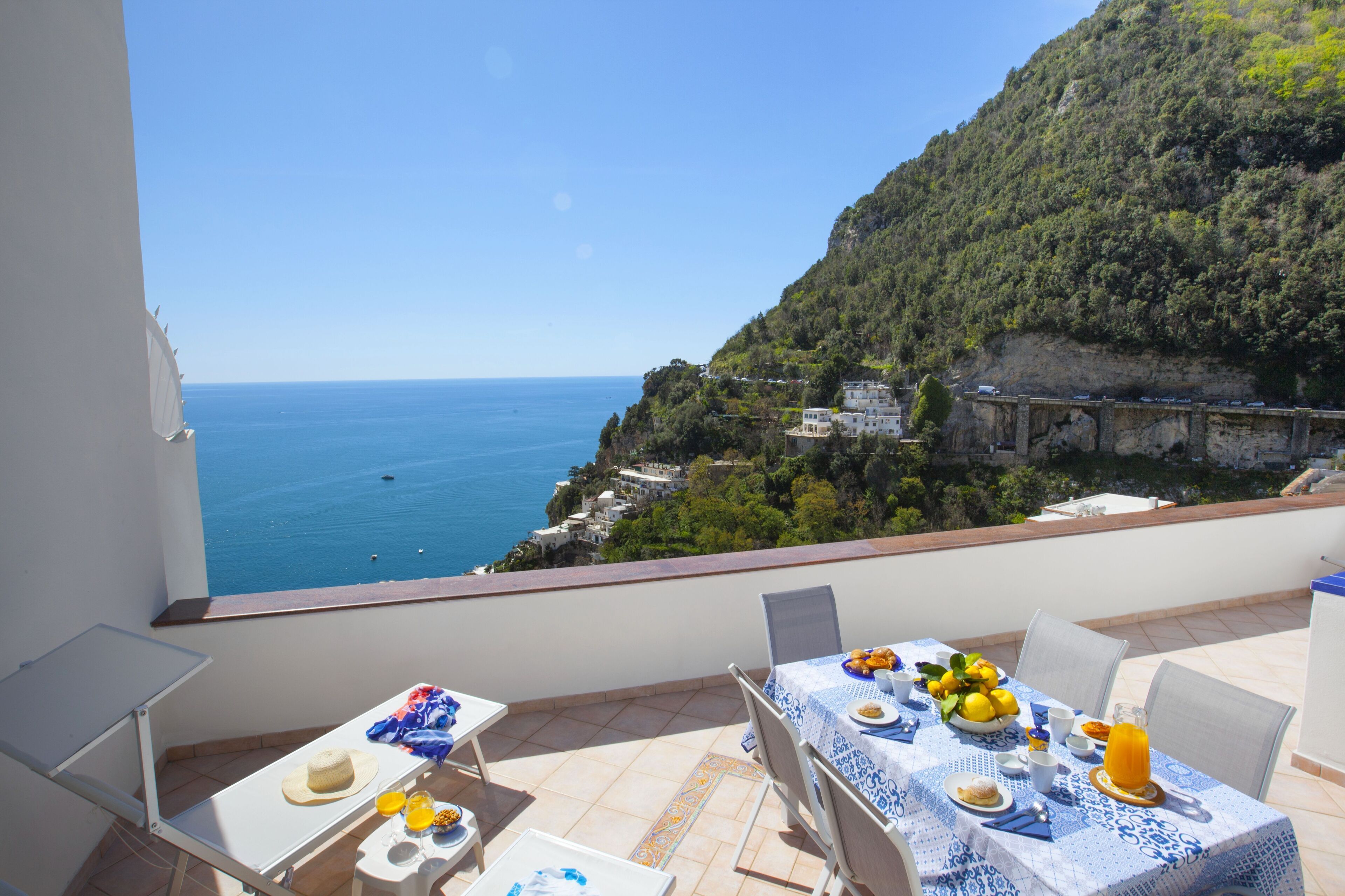 A balcony with a table set for breakfast overlooking a coastal view.