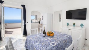 A room with a balcony, a table with a bottle and oranges, and a TV on the wall.