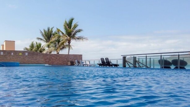 A swimming pool with lounge chairs and palm trees in the background. - Depas Tramonto (Mazatlán)