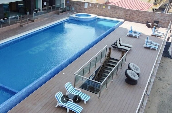 A rooftop swimming pool with lounge chairs and a small hot tub.