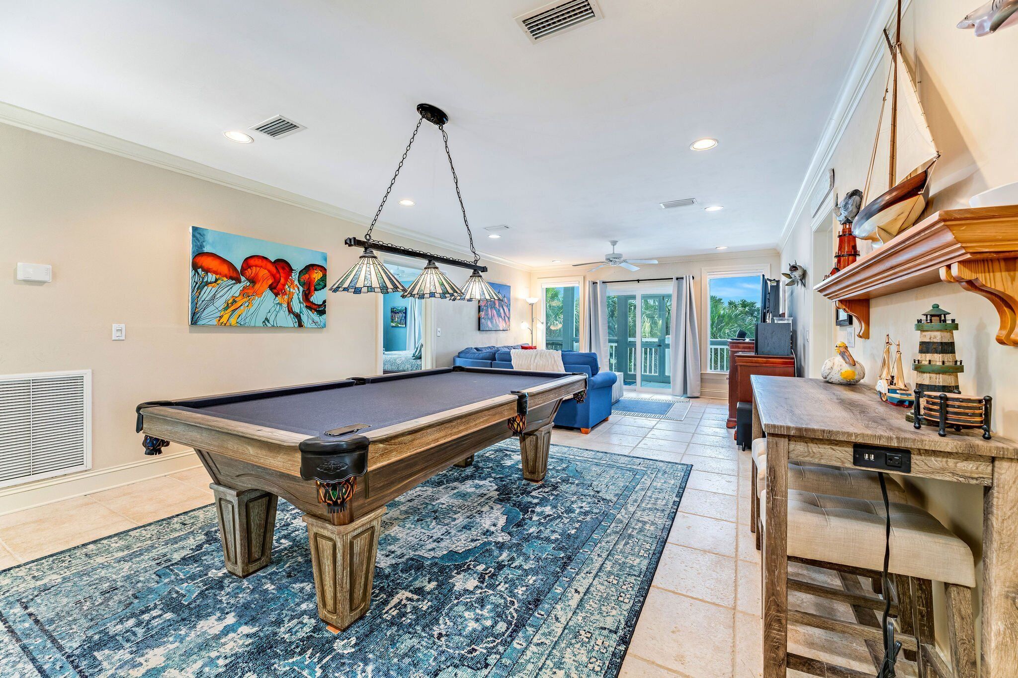 A pool table in a well-lit room with a large rug, a painting on the wall, and a wooden shelf with decorative items.