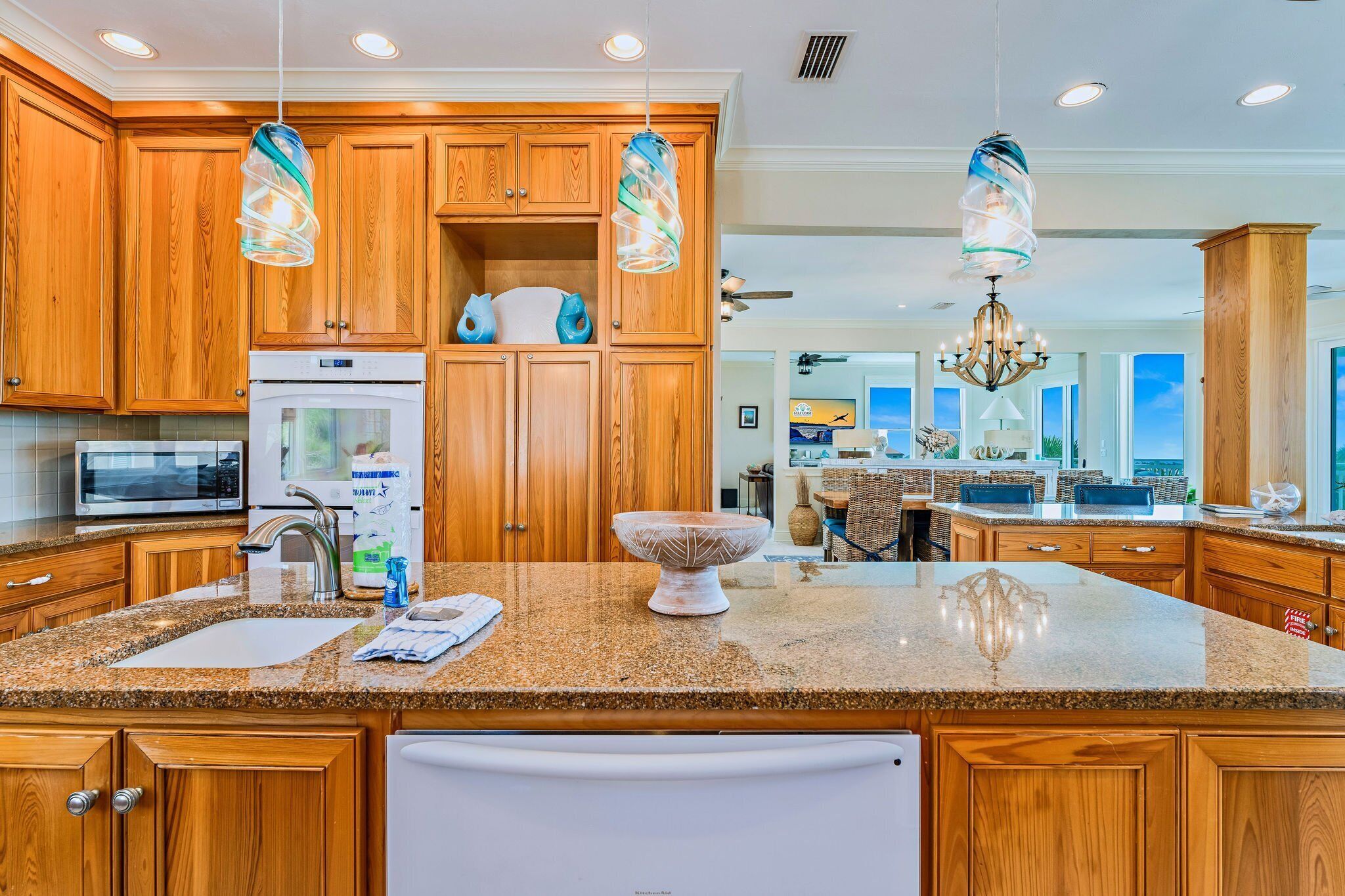 A kitchen with wooden cabinets, granite countertops, a built-in oven, and pendant lights.