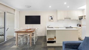 Una cocina moderna con armarios blancos, una pizarra y un comedor con mesa de madera y sillas blancas.