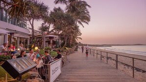 Un malecón de madera que lleva a una playa con palmeras y un bistró.