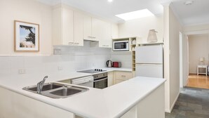 Una cocina moderna con armarios blancos, horno empotrado, microondas y pileta de acero inoxidable.
