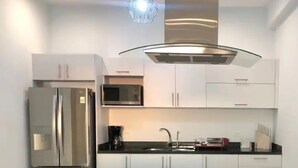 A modern kitchen with stainless steel appliances, white cabinetry, and a sleek black countertop. - Condos TT (Mazatlán)