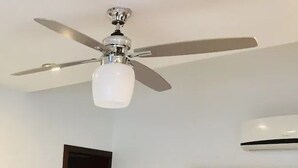 A ceiling fan with a light fixture in a room with white walls and an air conditioning unit. - Condos TT (Mazatlán)