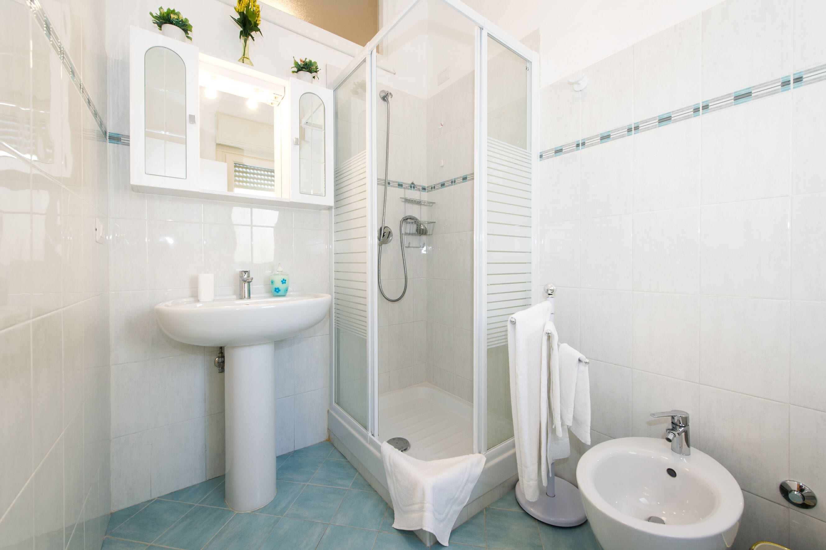 A bathroom with a glass-enclosed shower, a pedestal sink, and a bidet.