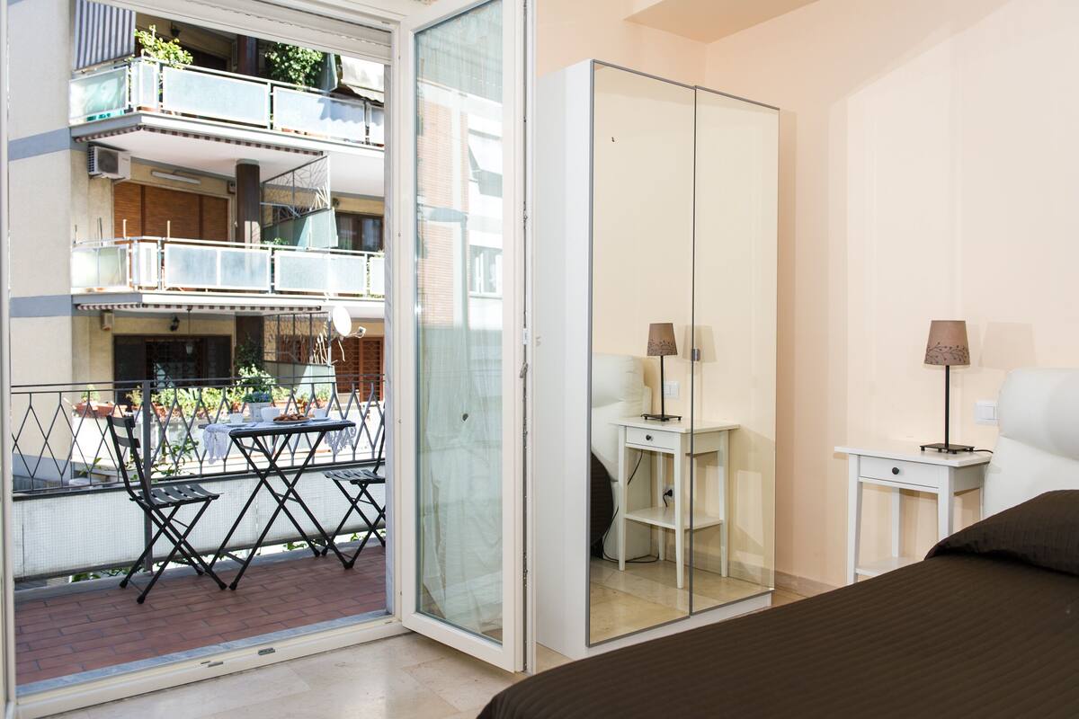 Quarto com uma grande porta de correr que dá para uma varanda com mesa e cadeiras.