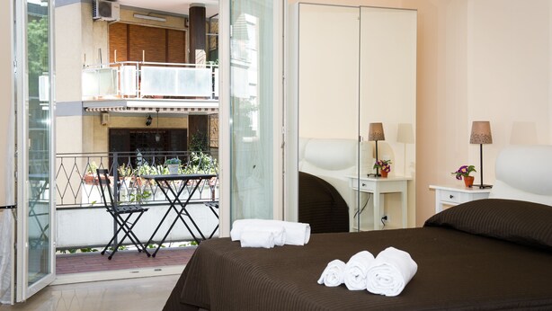 A hotel room with a bed, a small desk, a chair, a balcony with a table and chairs, and a view of the outside. - GREGORY BIG FAMILY (Rome)
