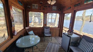 Eine Holzterrasse mit einem Glastisch und Stühlen, mit Blick auf einen See.