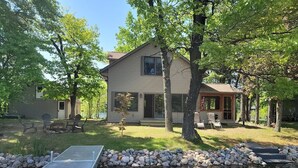 Ein Haus mit einem Steg, der in einen Teich führt, umgeben von Bäumen und einem grünen Rasen.